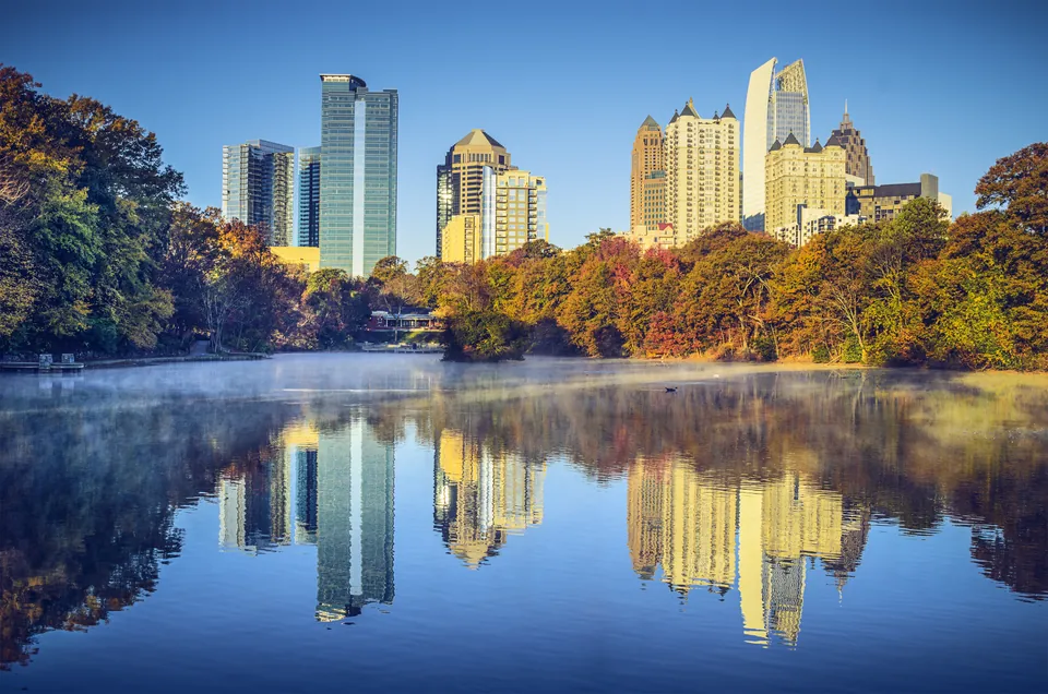 Atlanta's Midtown skyline reflected in the lake at Piedmont Park, framed by autumn trees.